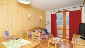 A wooden-paneled room with a sofa, a dining table, a television, and a window with red curtains. - Résidence Odalys Le Grand Panorama 1 (Valmeinier)