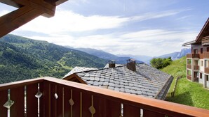 A chalet with a stone roof, wooden balcony, and mountain views. - Résidence Odalys Le Grand Panorama 1 (Valmeinier)