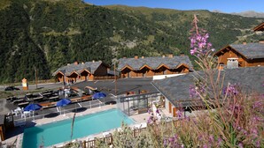 A mountain resort with wooden chalets, a swimming pool, and a view of the surrounding hills. - Résidence Odalys Le Grand Panorama 1 (Valmeinier)