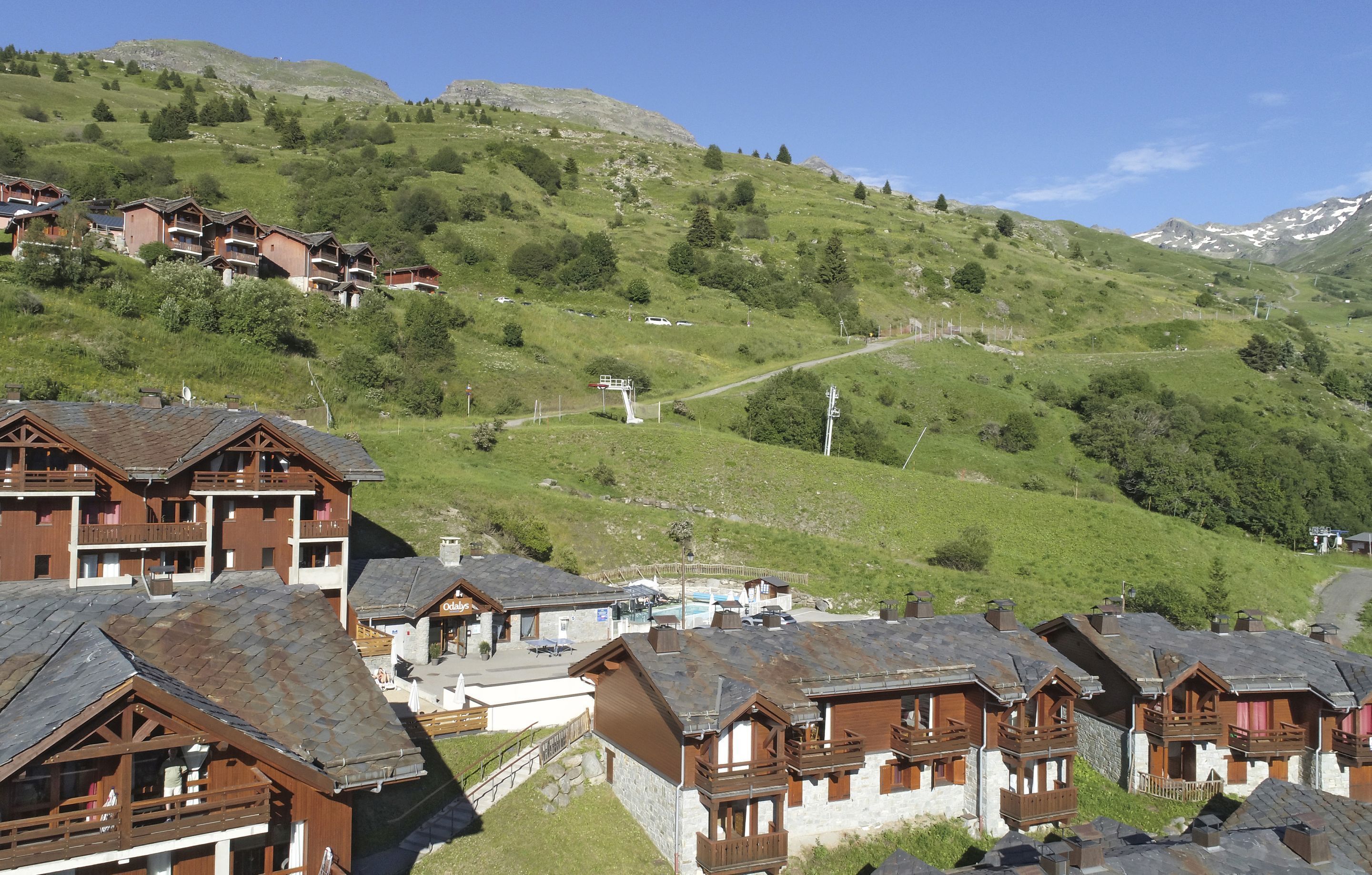 Uma estância de montanha com edifícios em estilo chalé, um teleférico e uma área de piscina.