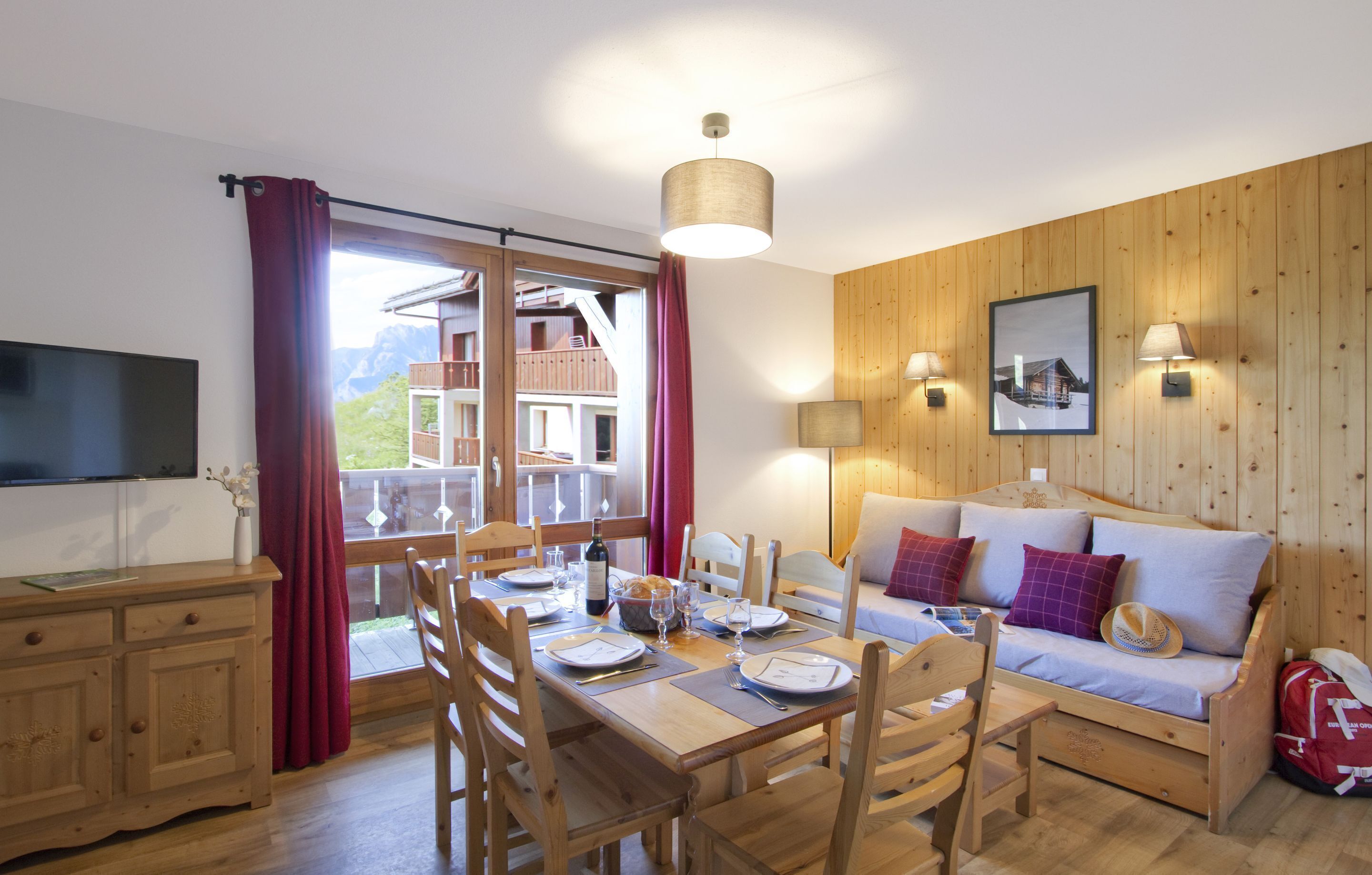 A dining area with a wooden table set for four, a sofa with cushions, and a television on the left.
