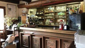 A bar area with wooden counter, shelves with bottles and glasses, and a refrigerator. - Hotel Restaurant Le Ranch de Turini (La Bollene-Vesubie)