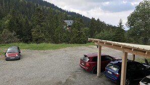 A gravel parking area with several cars parked under a wooden shelter. - Hotel Restaurant Le Ranch de Turini (La Bollene-Vesubie)
