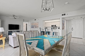 A modern living room with a large dining table, a TV, and a kitchen in the background.