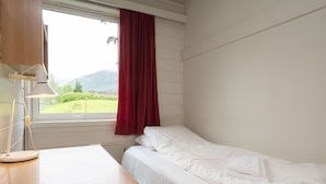 A room with a single bed, a wooden desk, a lamp, and a window with a red curtain. - Førde Sommarhotell (Sunnfjord)