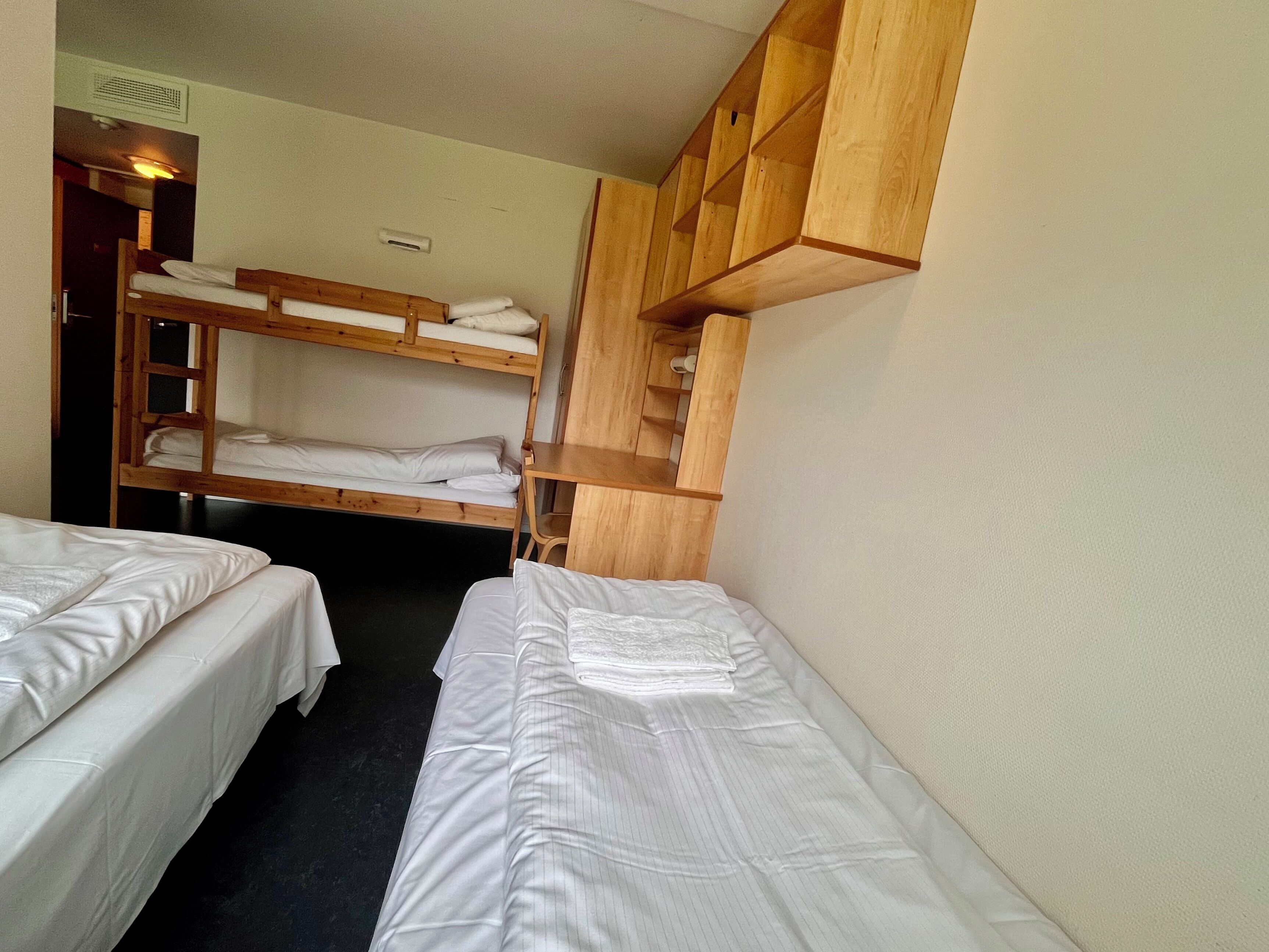 A room with two single beds, a bunk bed, and a wooden wardrobe.