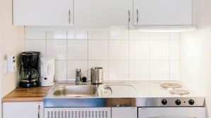 A compact kitchen with white cabinets, a stainless steel sink, a coffee maker, a kettle, a grater, and a microwave. - Førde Sommarhotell (Sunnfjord)