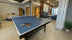 A ping pong table with a paddle in a modern indoor space with a brick wall, wooden ceiling, and a seating area with a sofa and chairs. - Førde Sommarhotell (Sunnfjord)