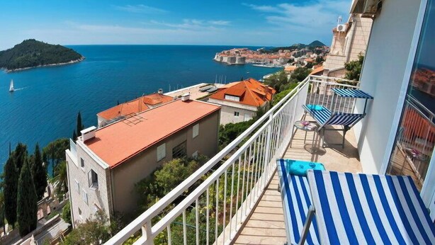 A balcony with a view of the sea, a small island, and a historic town in the distance. - Sipa Apartments (Dubrovnik)