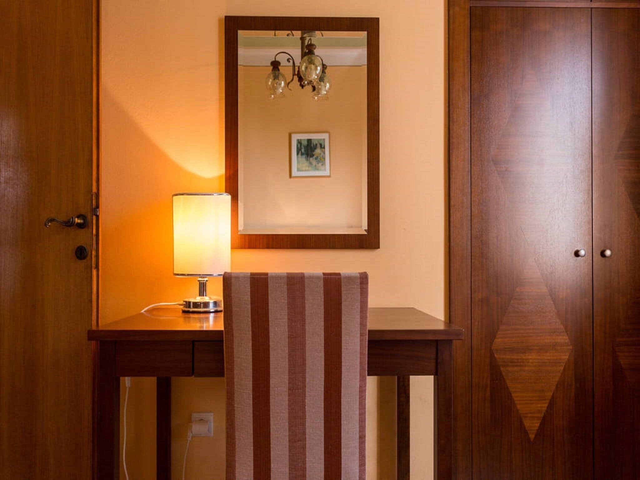 Un bureau en bois avec une lampe, une serviette à rayures, un tableau encadré et une porte en bois.