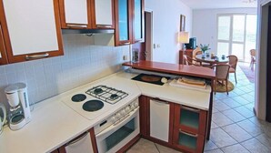 A compact kitchen with white cabinets, a gas stove, a coffee maker, and a dining area with a table and chairs. - Sipa Apartments (Dubrovnik)