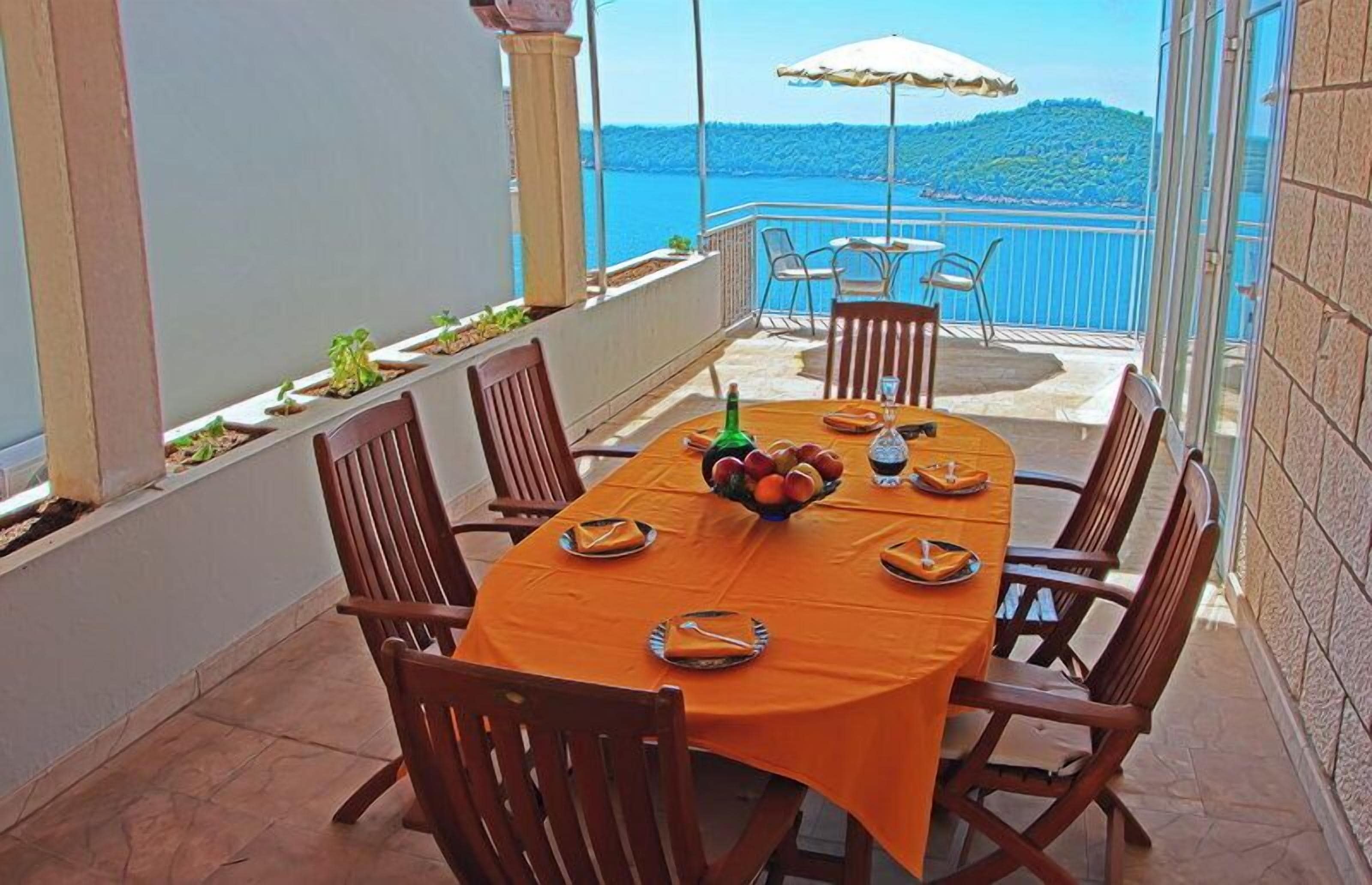 A dining table set for four with a fruit bowl, a bottle, and plates on an orange tablecloth.