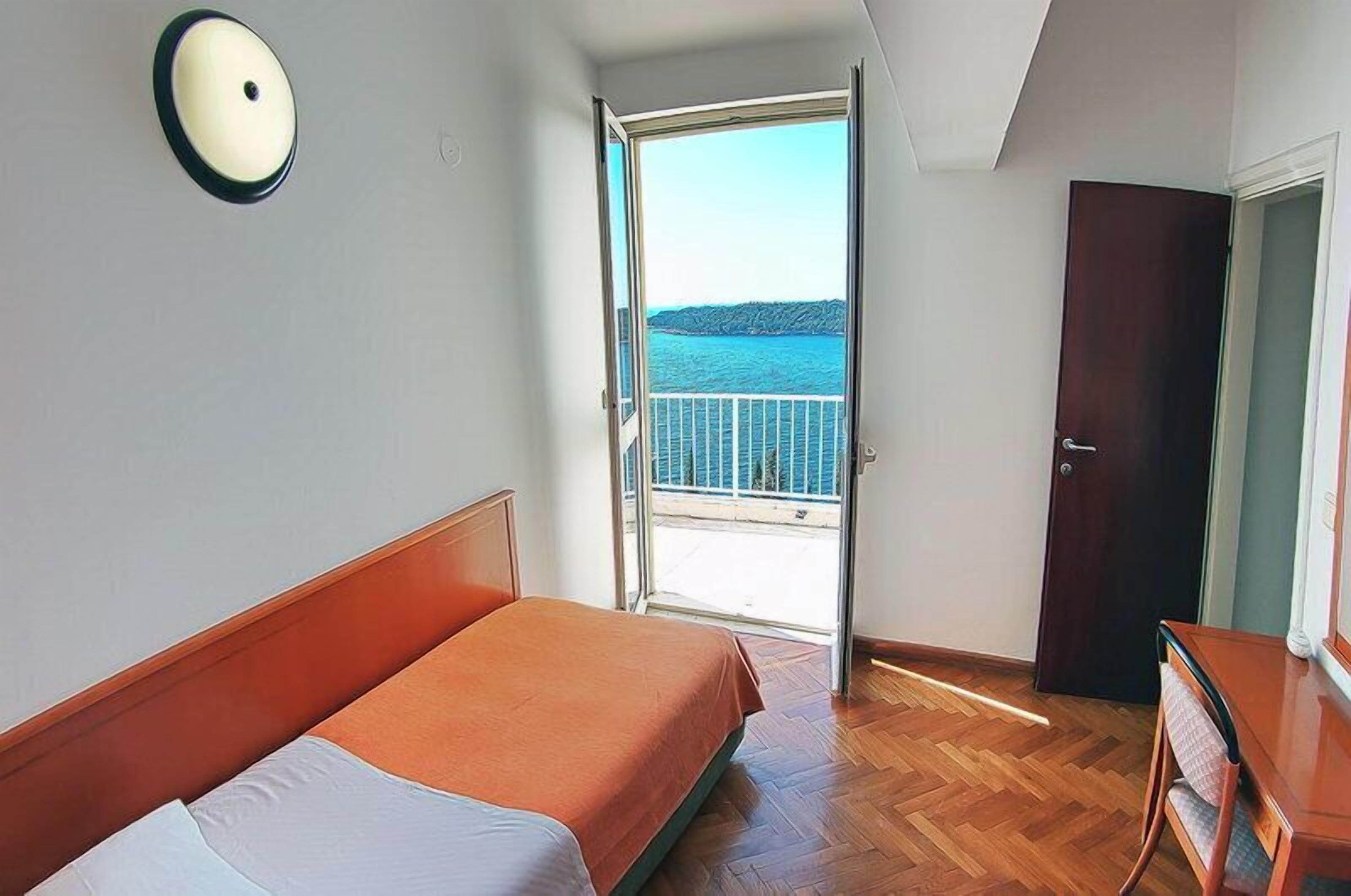 Ein Zimmer mit einem Bett, einem Holzkapfen, einer Tür und einem Balkon mit Blick aufs Meer.