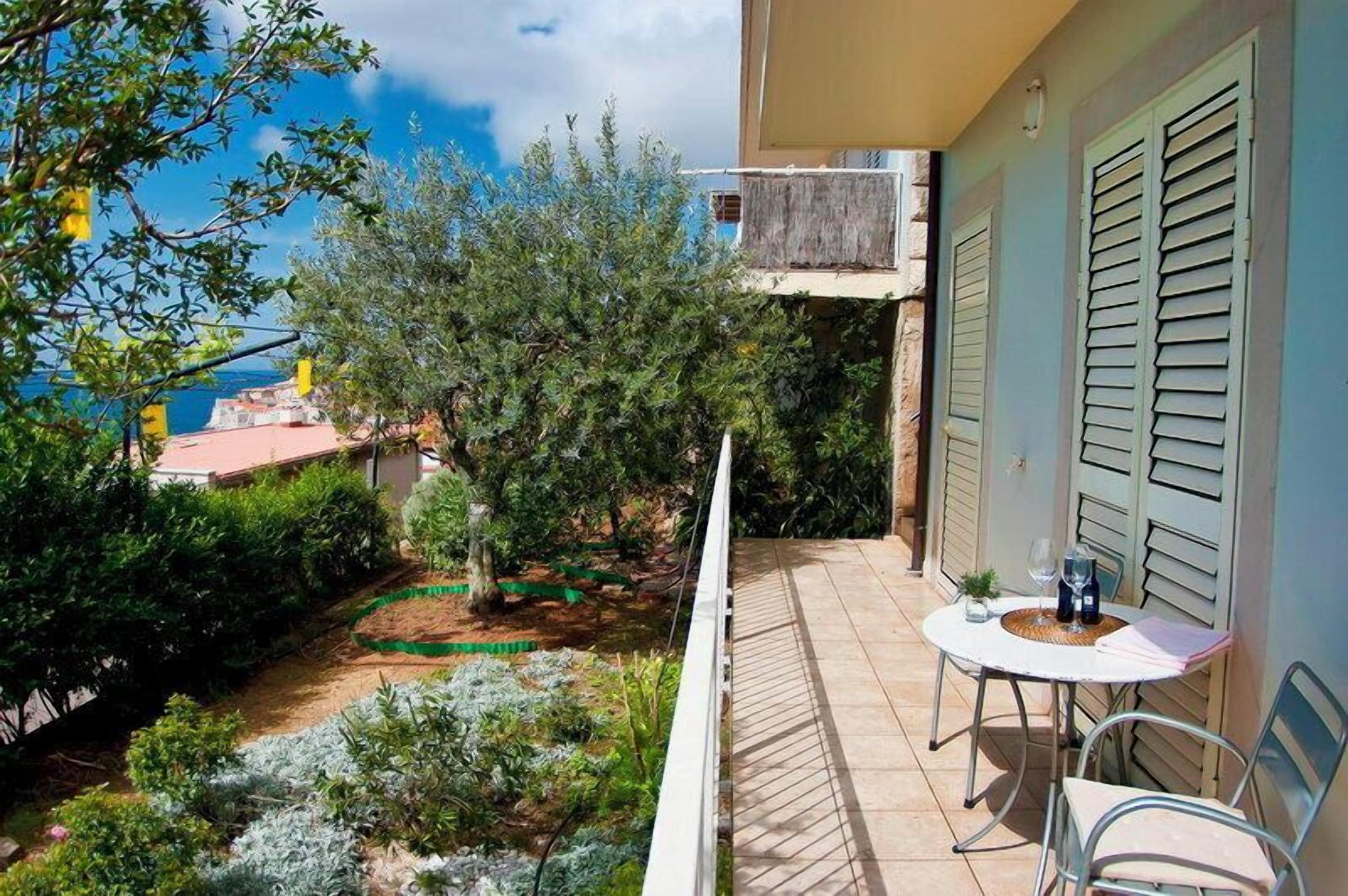 A balcony with a table and chairs, overlooking a garden and a view of the sea.