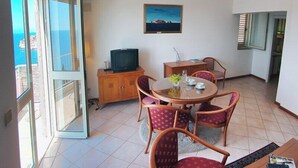 A balcony with a view of the sea, a dining area with a table and chairs, a television on a cabinet, and a painting on the wall. - Sipa Apartments (Dubrovnik)