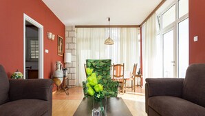 A living room with two sofas, a coffee table, and a patterned armchair. There is a lamp, a vase with flowers, and a window with curtains. - Sipa Apartments (Dubrovnik)
