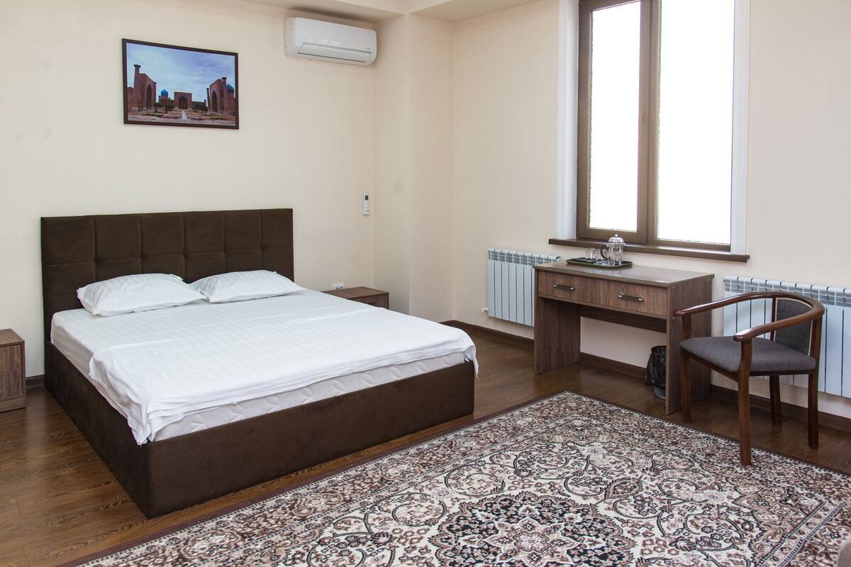 A bedroom with a bed, a desk, a chair, a radiator, and a window.