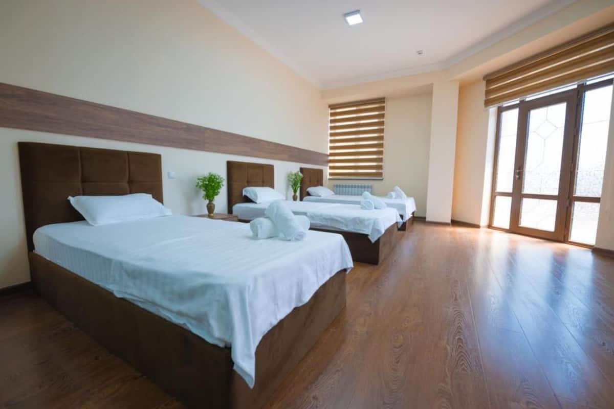 A hotel room with two beds, wooden flooring, and large windows.