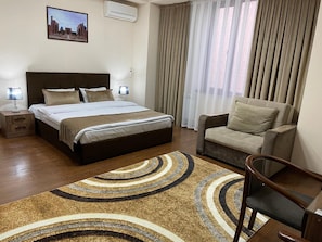 A hotel room with a large bed, a sofa, a chair, a nightstand, and a rug. - Meros Boutique Hotel (Tashkent)