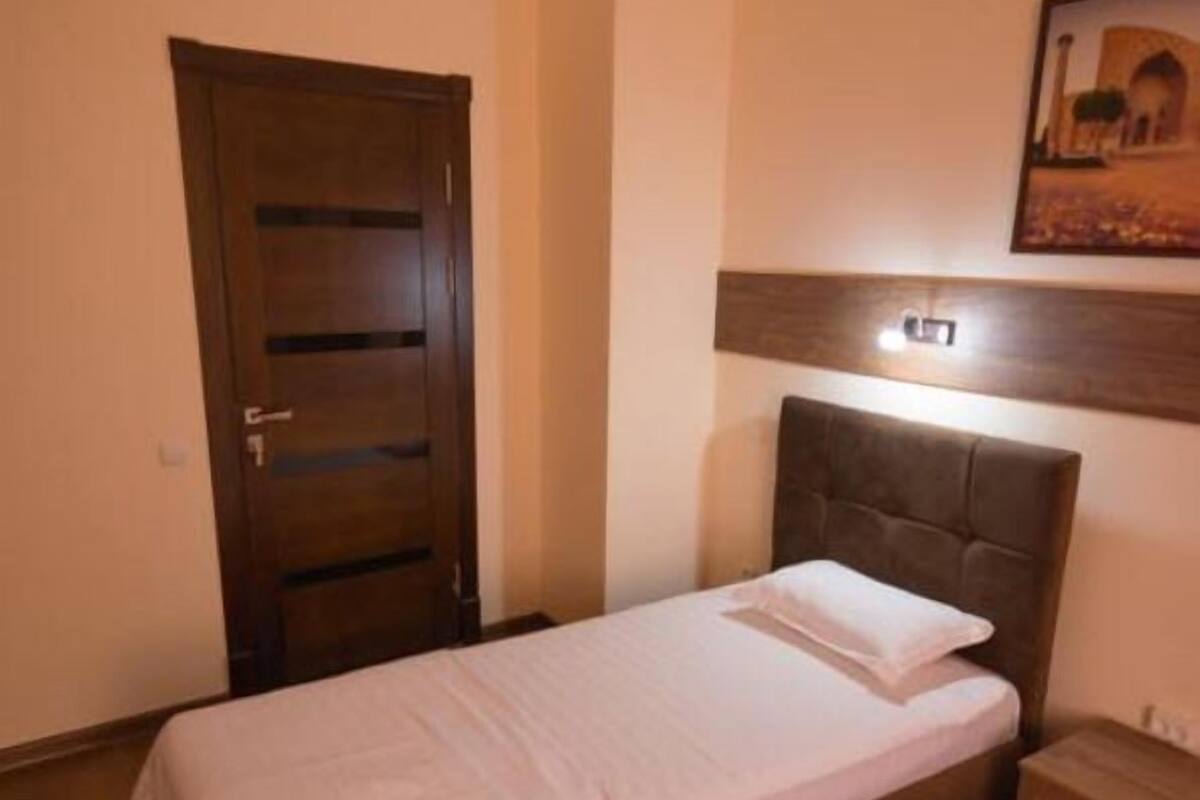 A single bed with a wooden headboard and a nightstand, a wooden door, and a framed picture on the wall.