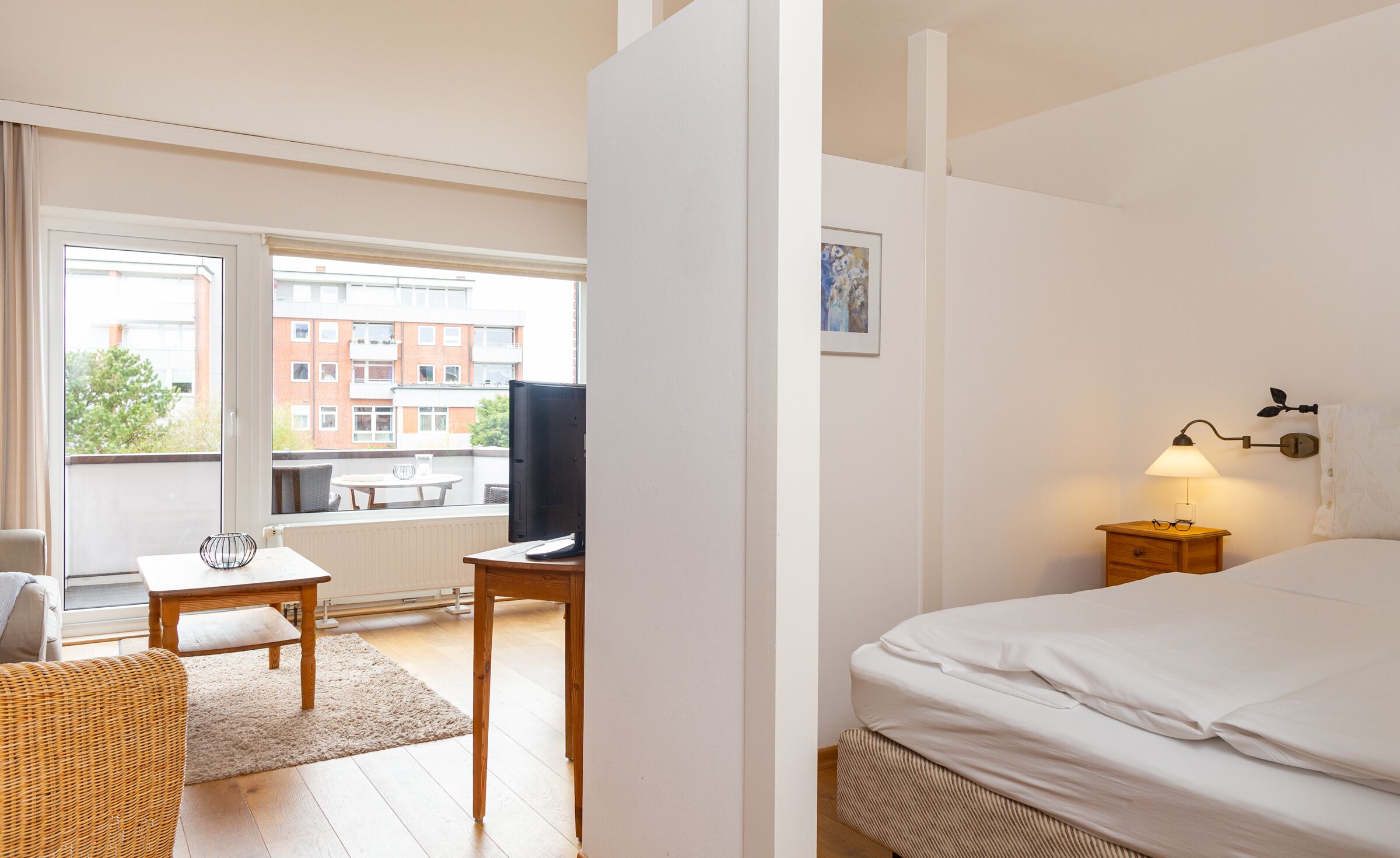 Ein Hotelzimmer mit Bett, Schreibtisch, Stuhl, Tisch, Fernseher und einem Fenster mit Blick auf Gebäude.