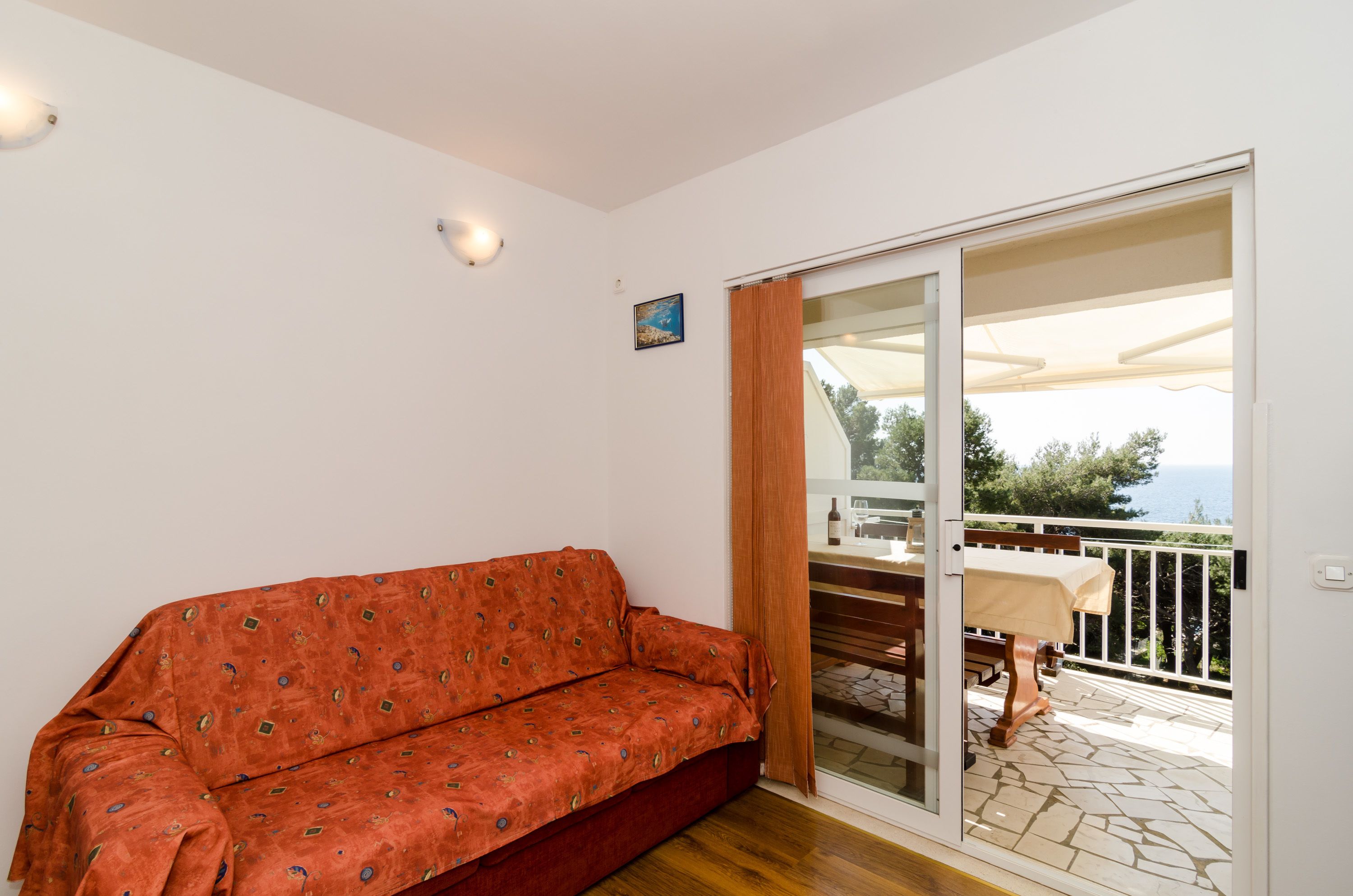 Un sofá rojo en una habitación con un ventanal corredero que da a un espacio exterior con una mesa y sillas.