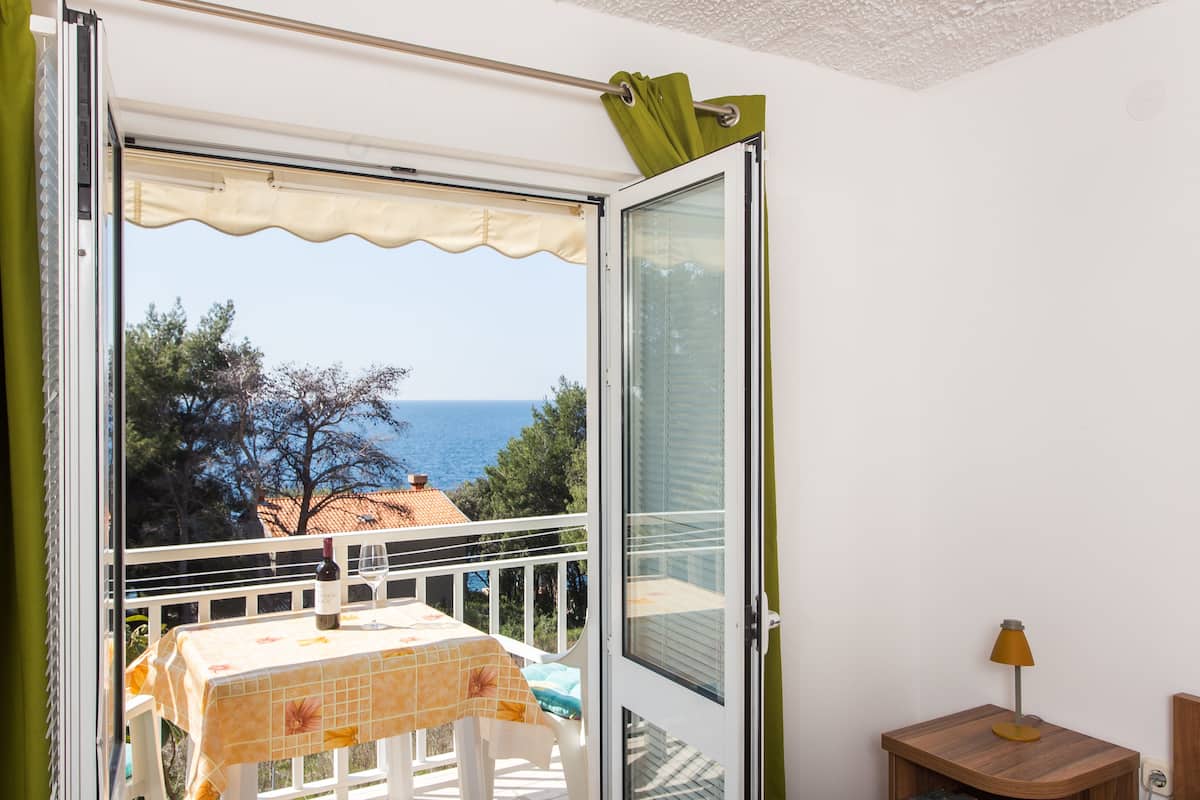 Un balcon avec une table et des chaises, une vue sur la mer et une table de chevet en bois avec une lampe.