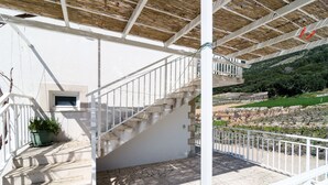 A covered outdoor area with stone steps leading to a white railing, a potted plant, and a view of a hillside. - Apartments Villa Ana - Dingac (Orebic)