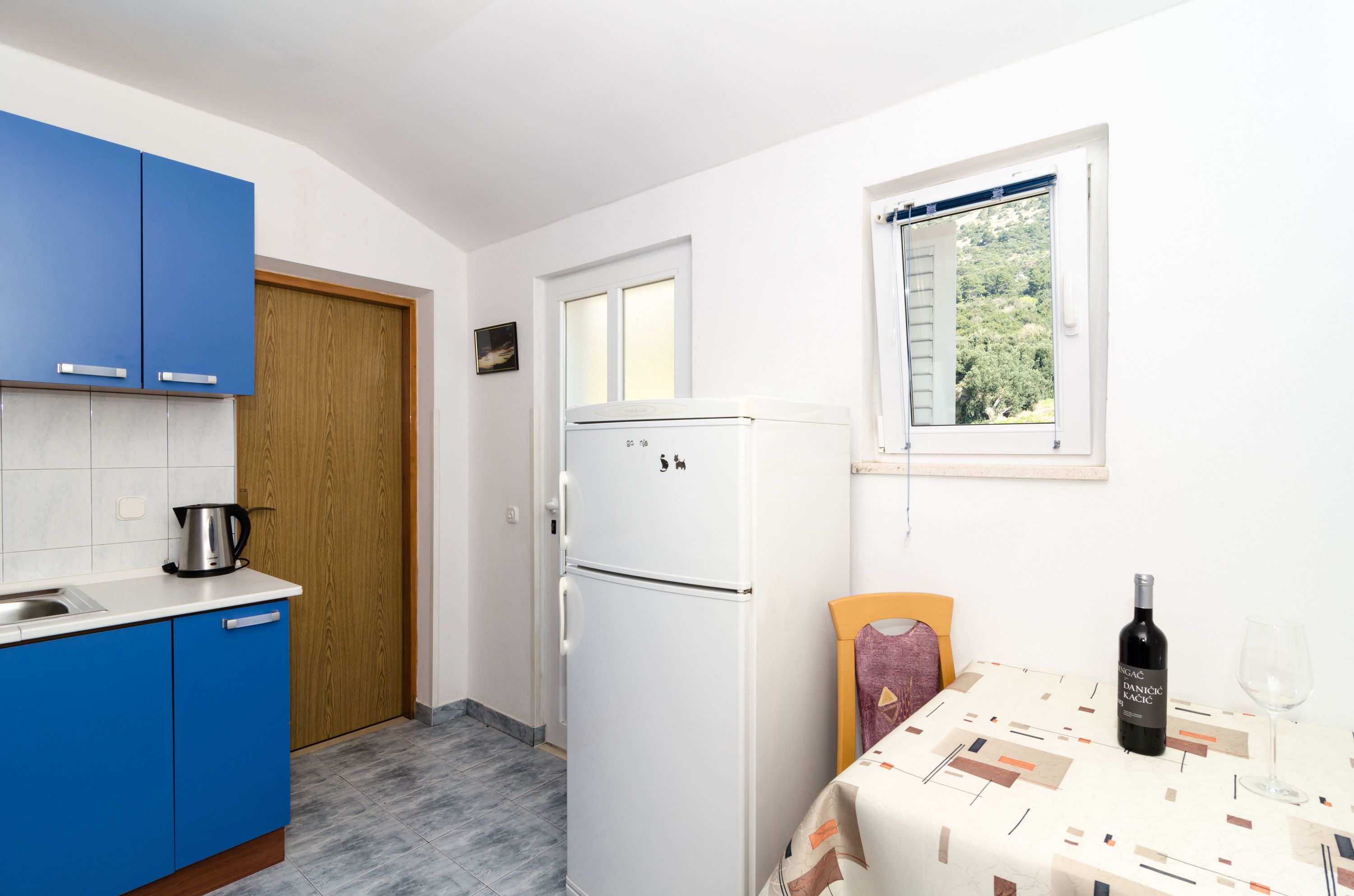 Une cuisine compacte avec des meubles bleus, un réfrigérateur blanc et un coin repas avec une table dressée pour deux personnes.