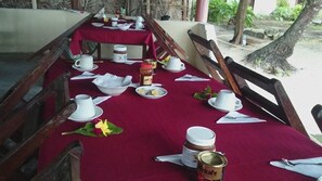A dining table set with white cups, saucers, plates, and utensils, covered with a red tablecloth.