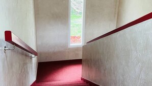 A narrow stairway with a red handrail and a window at the top.