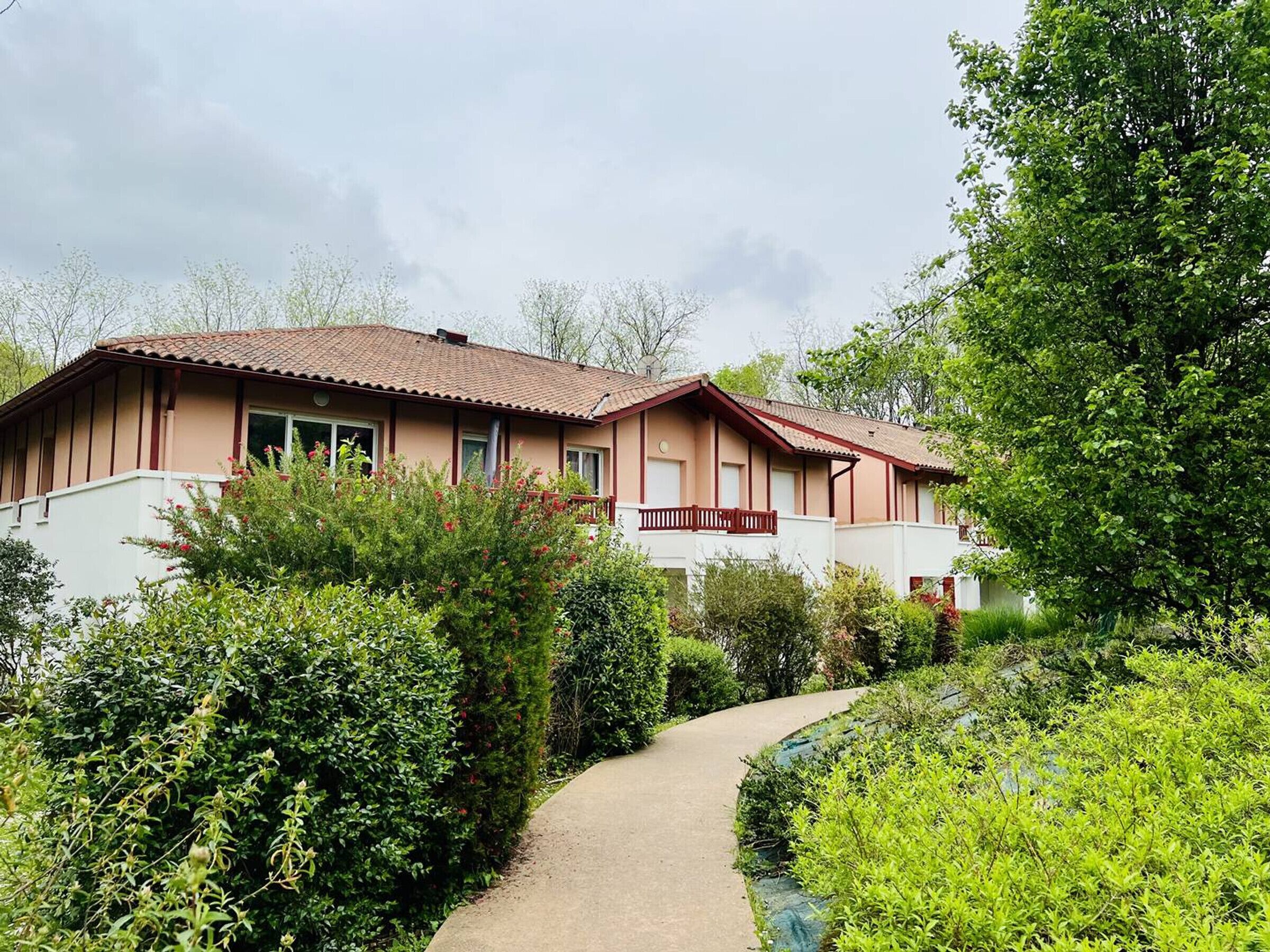 A two-story house with a red-tiled roof, a balcony, and a pathway leading to the entrance.