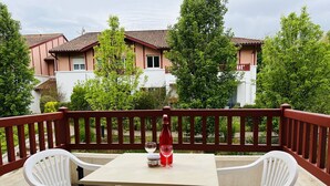 A balcony with a table and two chairs, a bottle of red wine, and a glass.