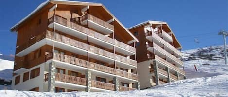 A multi-story hotel with balconies, set against a snowy mountain backdrop.