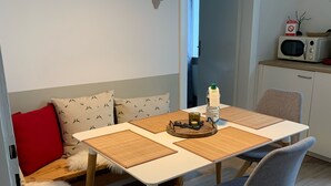 A modern dining area with a wooden table, two chairs, a bench with a fur throw, a hanging light fixture, and a microwave on a shelf.