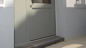A modern grey door with a glass panel, a metal handle, and a small step leading to the entrance.