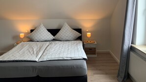 A neatly made bed with a headboard, two bedside lamps, and a window with curtains.