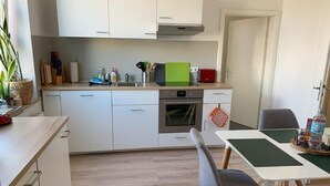 A modern kitchen with white cabinets, a built-in oven, and a dining area with a table and chairs.