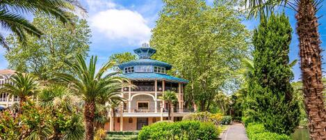Un edificio de estilo tradicional con techo azul, rodeado de exuberante vegetación y palmeras.