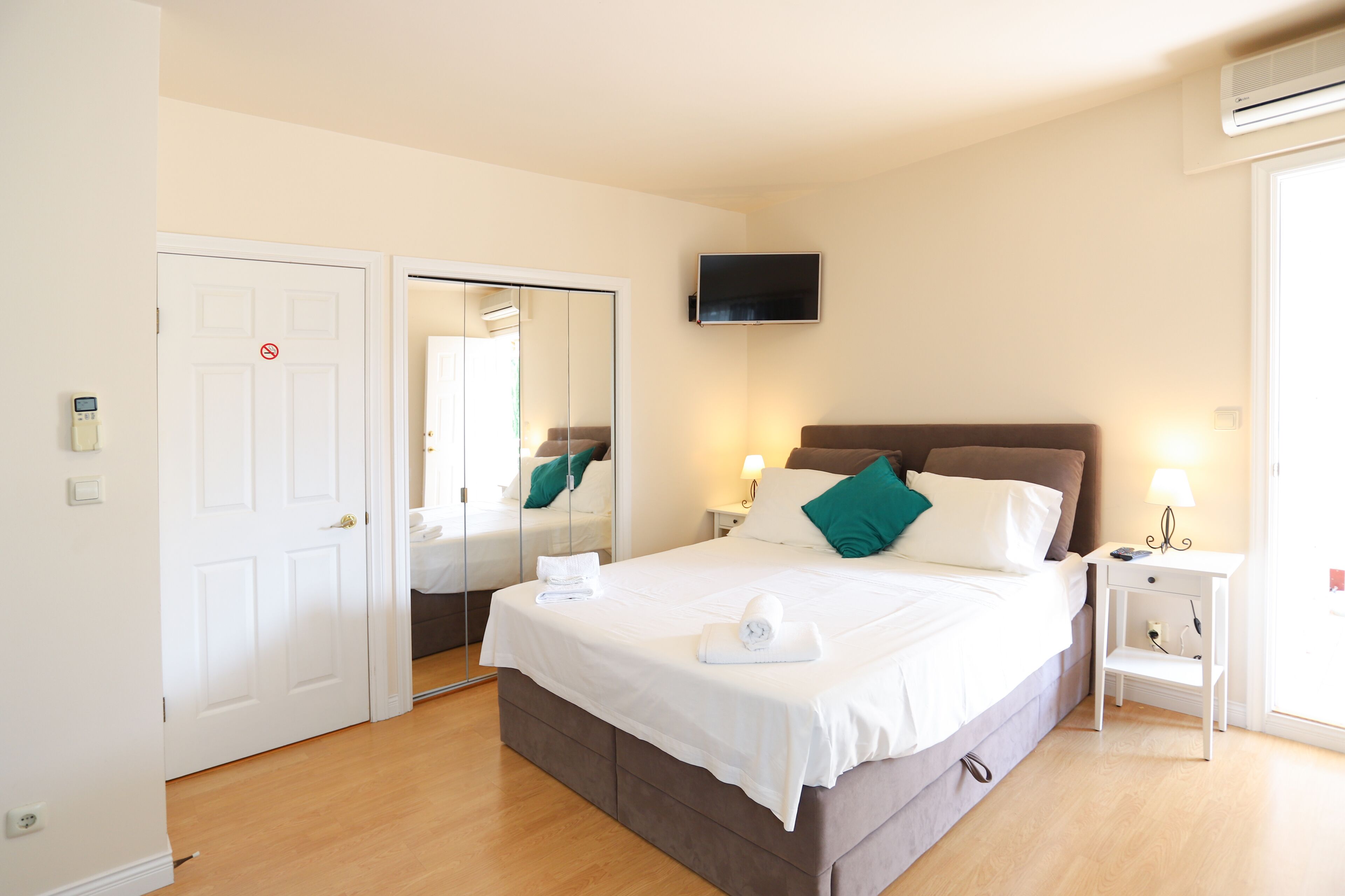 A neatly arranged bedroom with a bed, bedside tables, a TV, and a mirror.