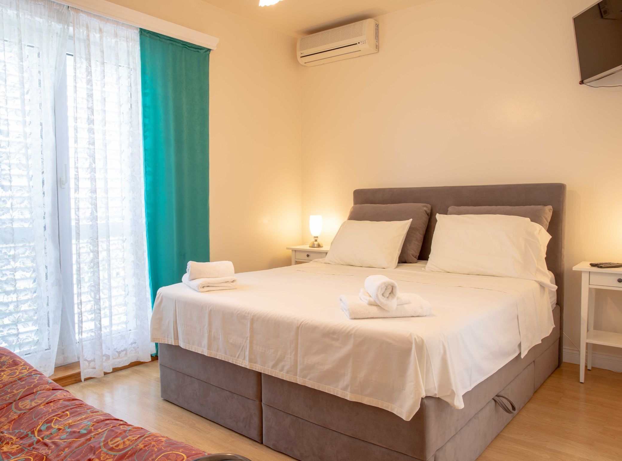 A hotel room with a bed, a bedside table, a lamp, and a window with curtains.
