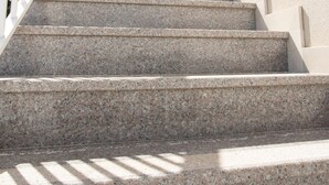 Un conjunto de escalones de piedra al aire libre que conducen a un edificio, con una barandilla blanca a la izquierda.