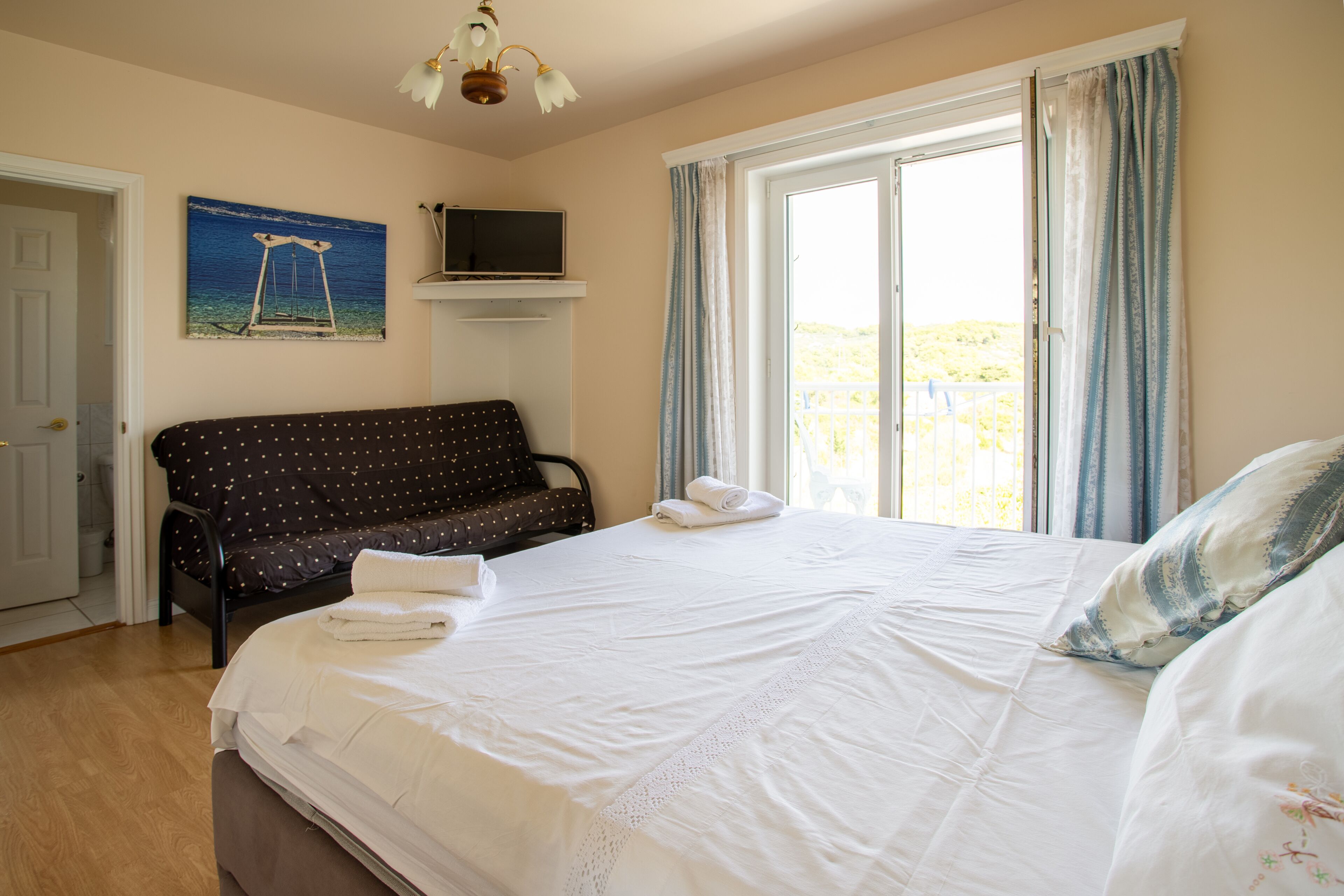 A bedroom with a bed, a bench, a painting, and a television on a shelf.