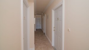 Un pasillo con puertas blancas, paredes color beige y piso de baldosas.