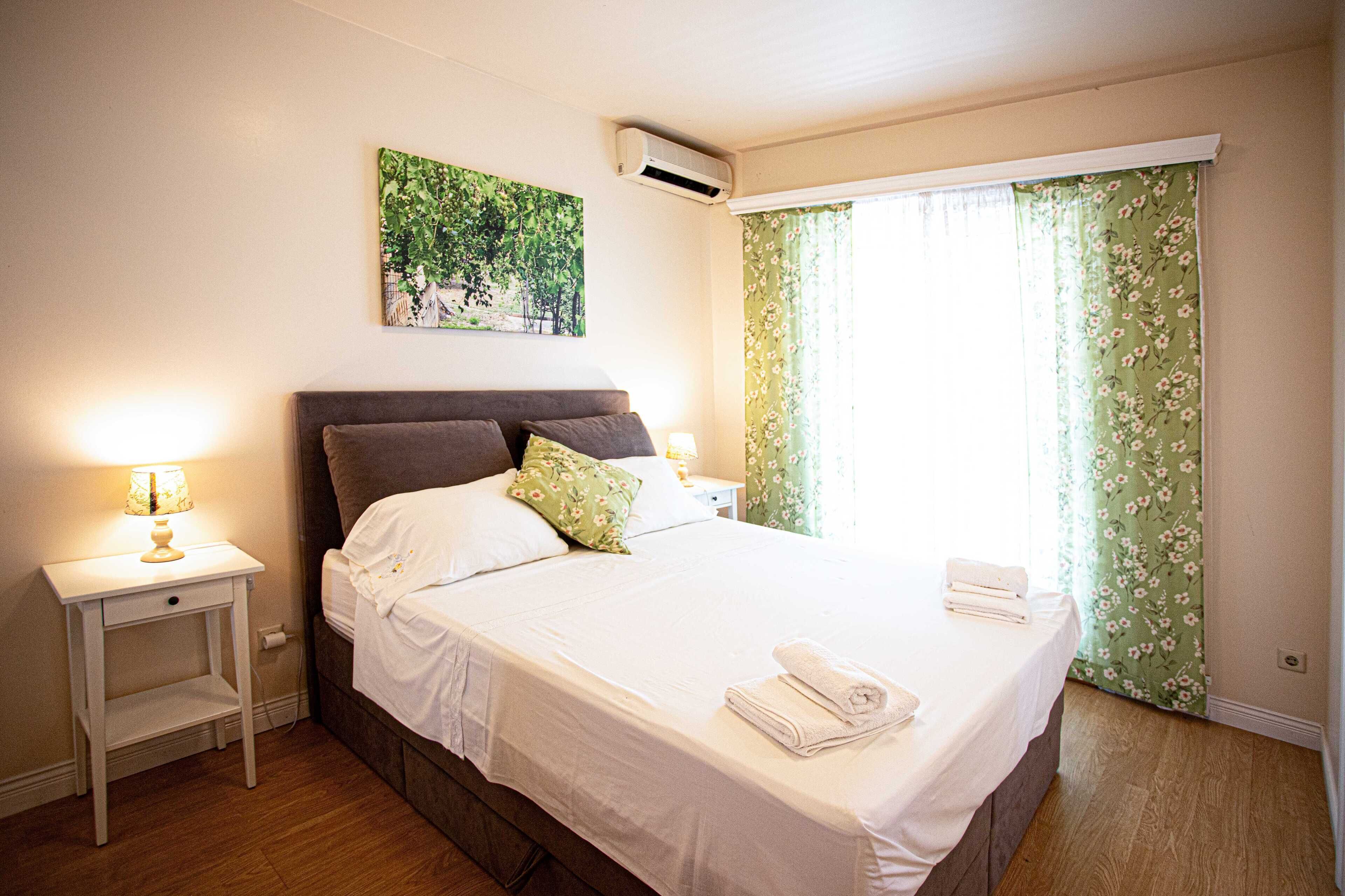 A neatly made bed with pillows, a bedside lamp, a small nightstand, and a wall-mounted air conditioner.