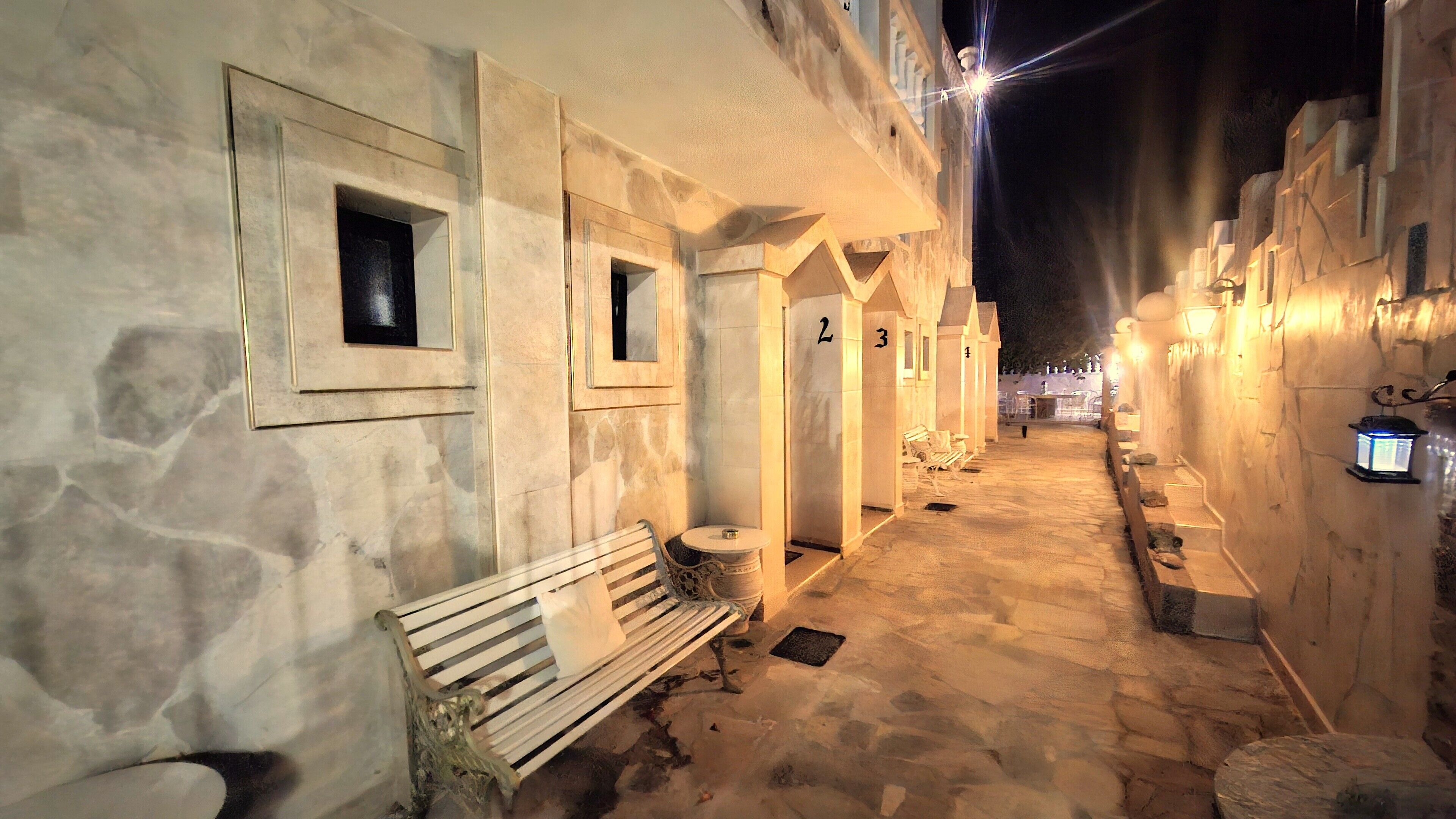 A narrow, stone-paved alleyway with benches and doors numbered 2 and 3.