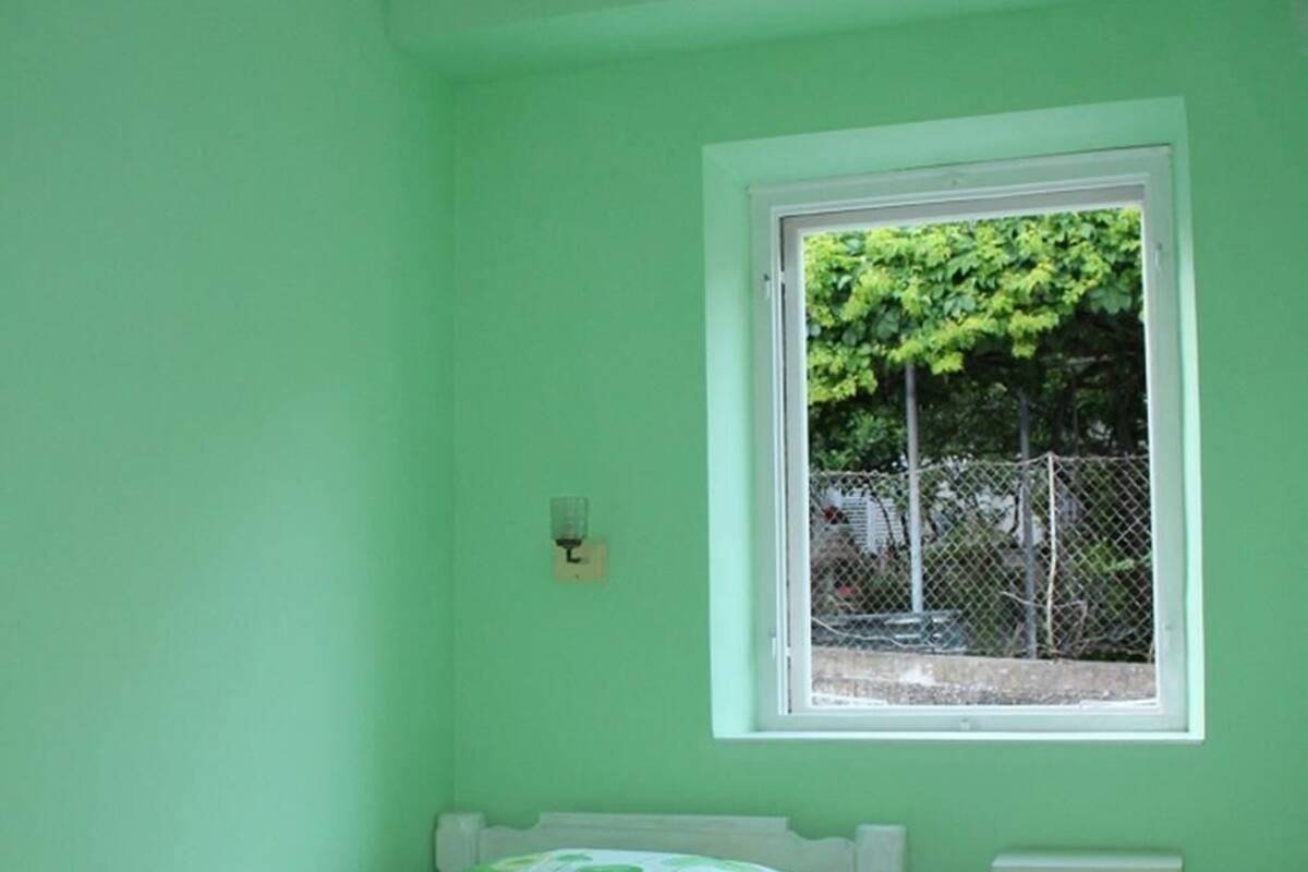 A room with a bed, a window, a nightstand, and a green wall.