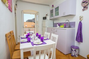 A compact kitchen with a microwave, sink, and cabinets. A dining table with chairs is set for four. - Guest House Gugily (Dubrovnik)