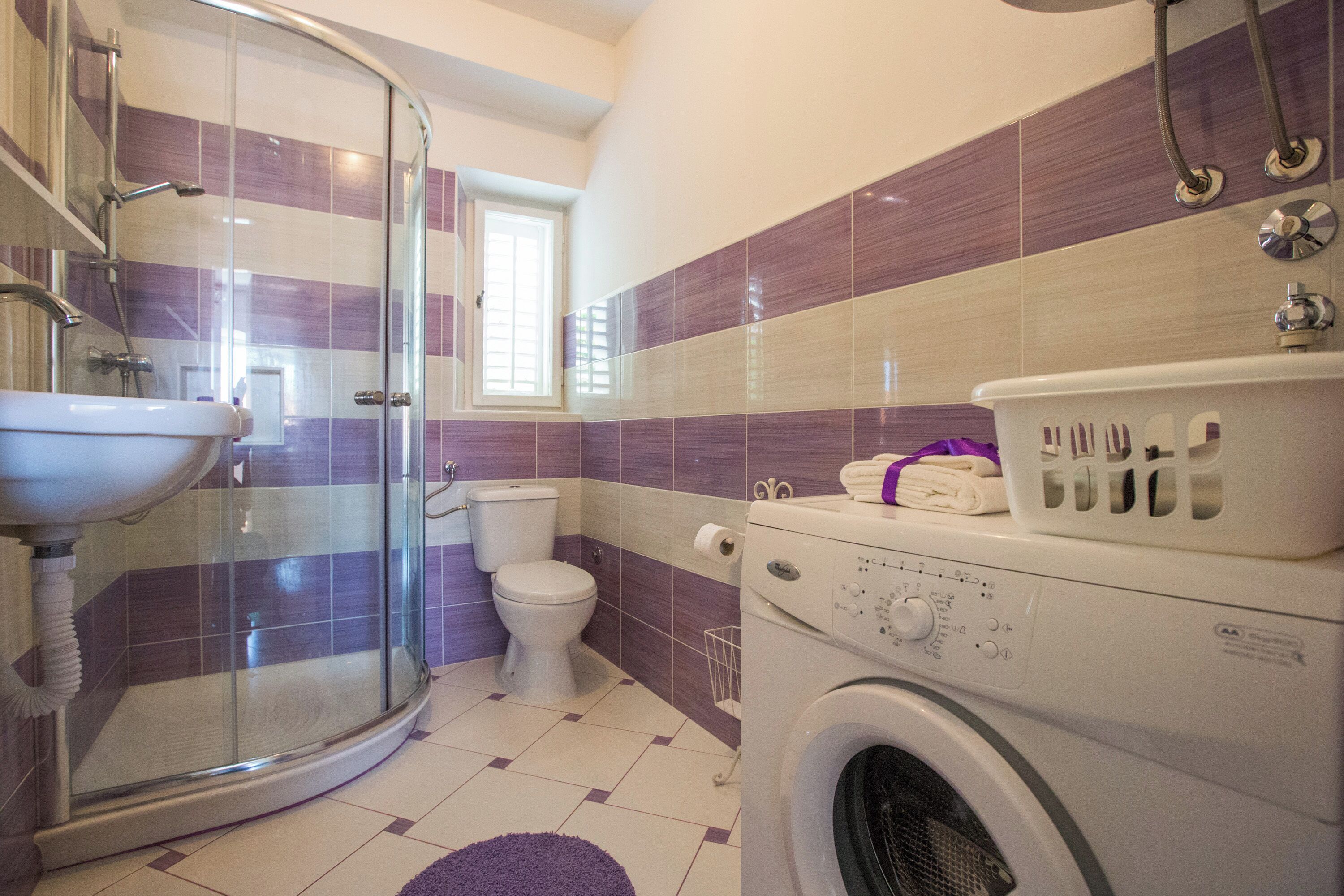 Un baño con cabina de ducha de vidrio, inodoro, lavadora y lavamanos.