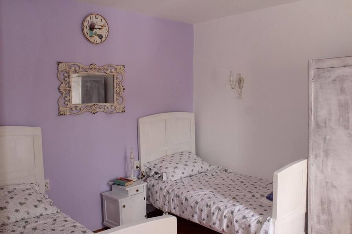A bedroom with two beds, a mirror, a clock, and a small bedside table.